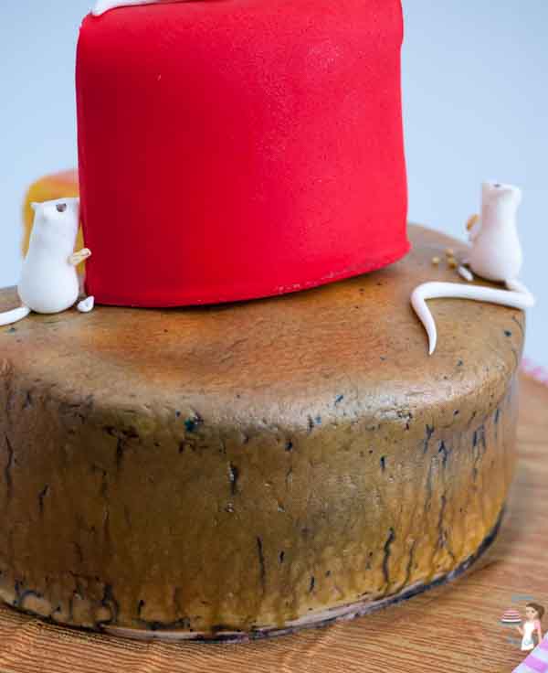 A close up of a cake decorated to look like three pieces of different cheeses.