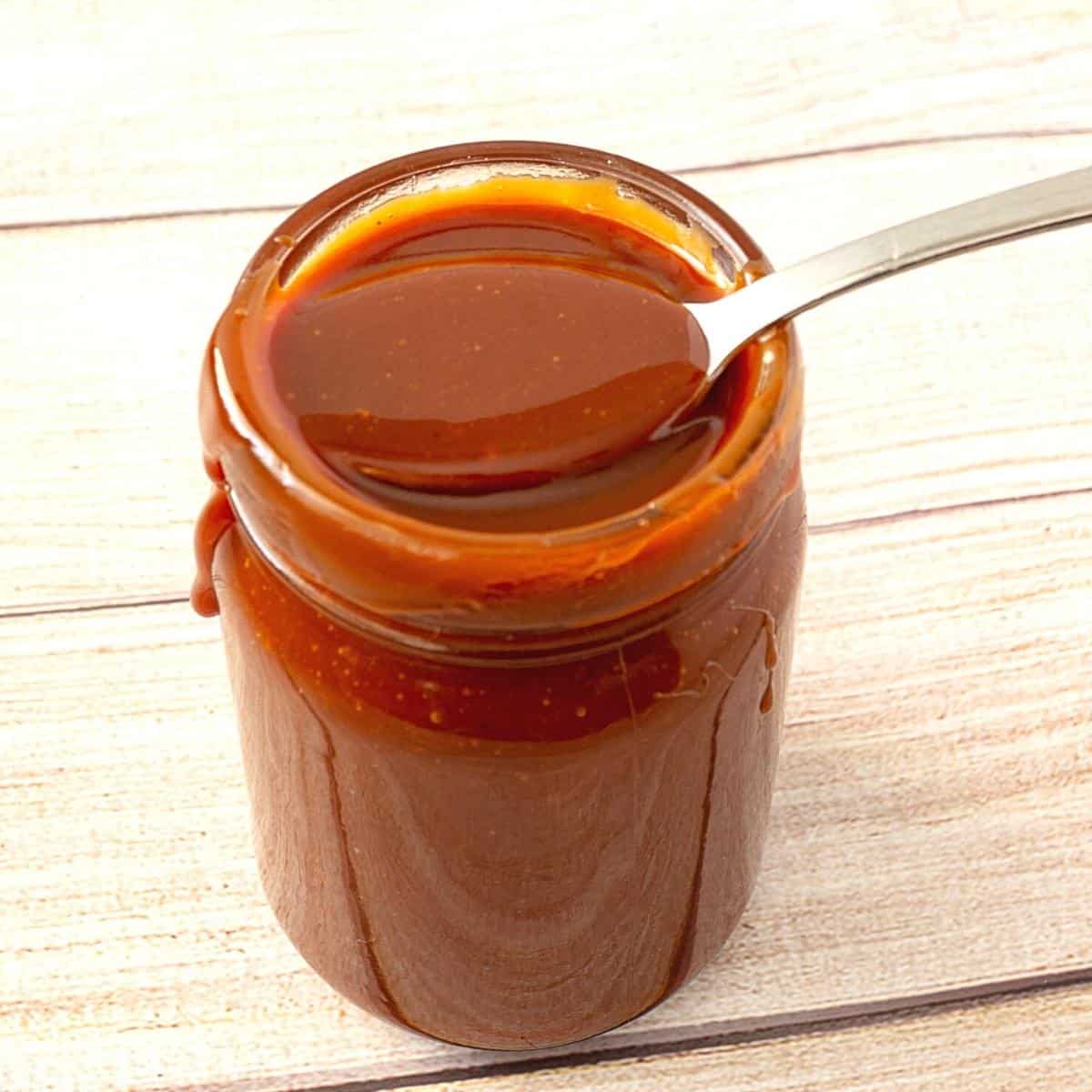 A mason jar and spoon with caramel.