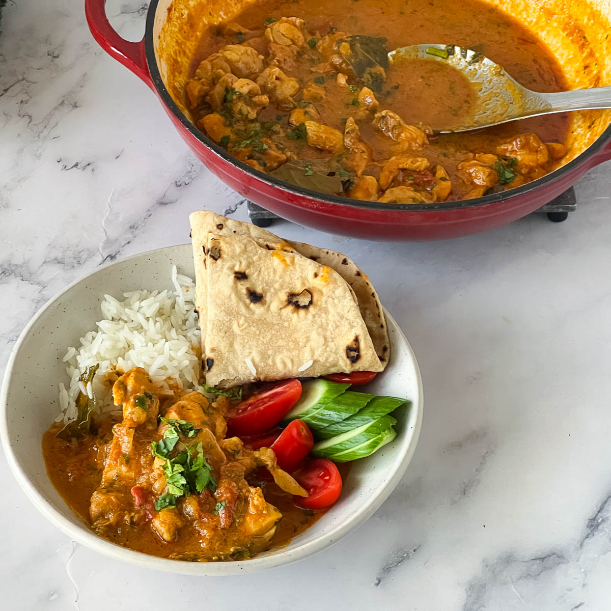 Curry chicken in a white plate with rice and chapati.