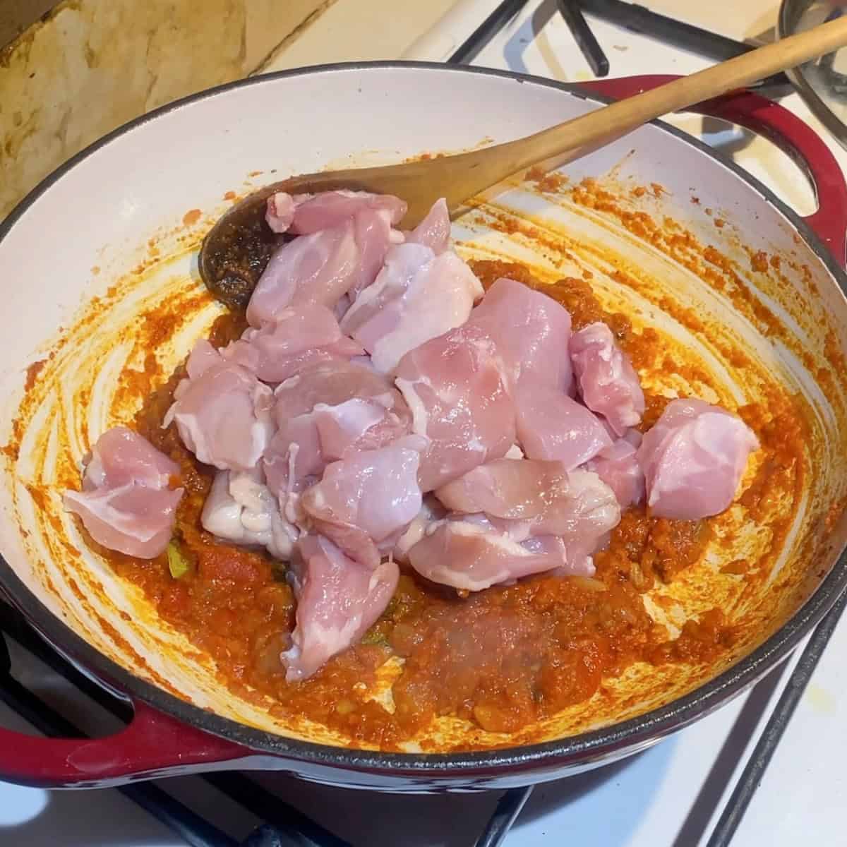 A skillet searing chicken for curry.