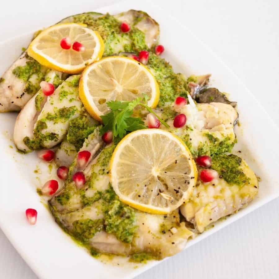 A serving platter with baked fish in cilantro marinade.