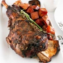 A bone in lamb shoulder roasted with veggies in a platter.
