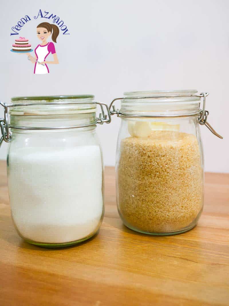A jar of white sugar next to a jar of brown sugar.