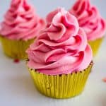 A pink Champagne buttercream frosted cupcake in a golden cupcake liner.