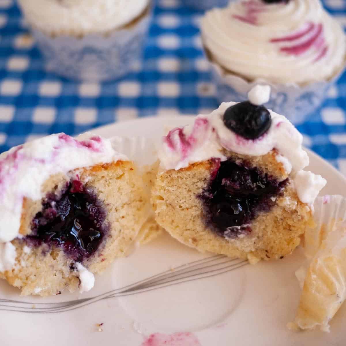 A frosted cupcake cut in half to show blueberry filling.