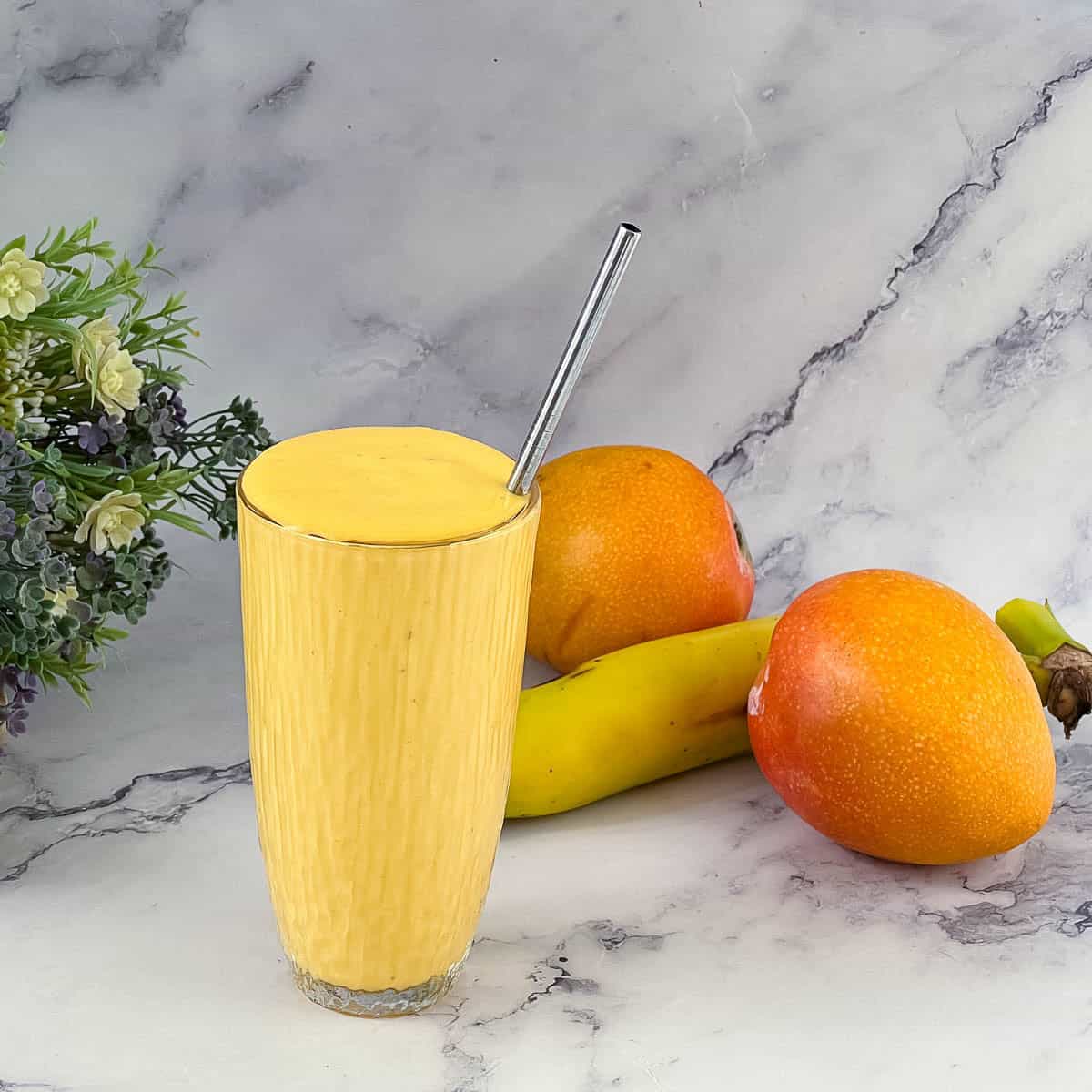 A tall glass with mango banana smoothie.
