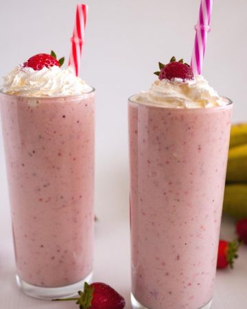 two glasses with milkshake, whipped cream, strawberry and a straw