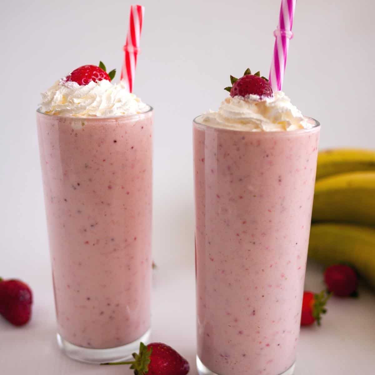 two glasses with milkshake, whipped cream, strawberry and a straw