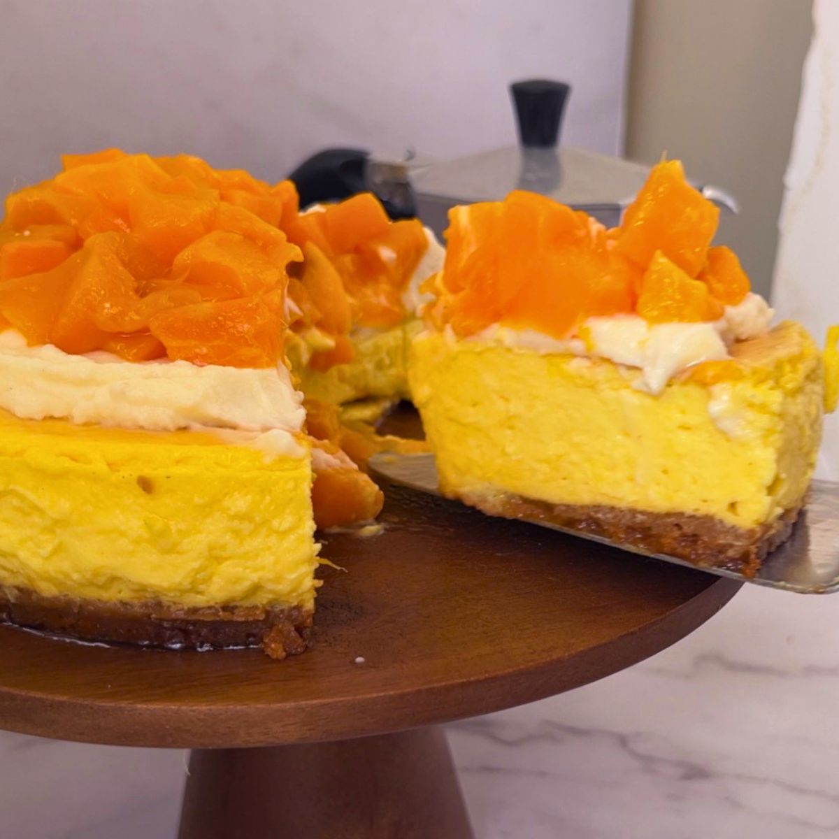 Slicing a mango cheesecake on cake stand.