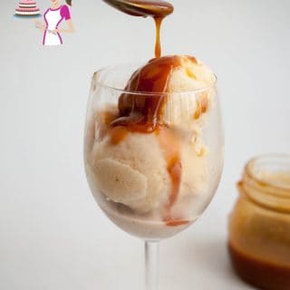 Two scoops of banana ice cream in a wine glass topped with caramel sauce