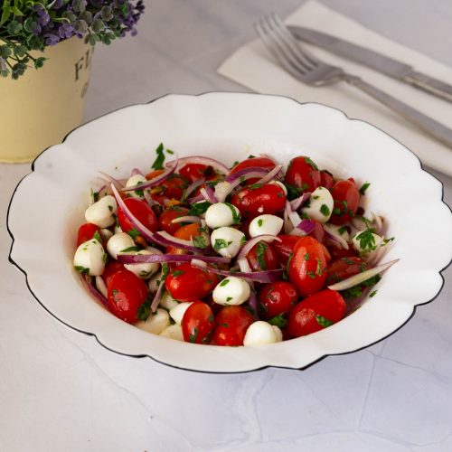 A white bowl with cherry tomato mozzarella salad.