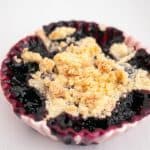 A ramekin with fruit crumbles blackberries.