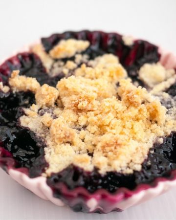 A ramekin with fruit crumbles blackberries.
