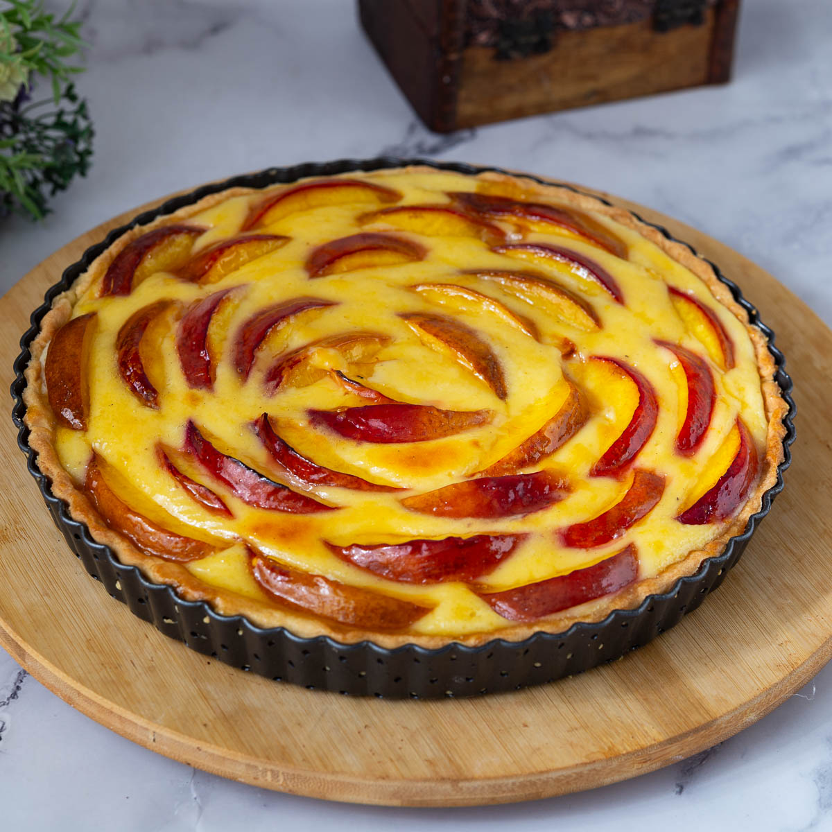 A baked nectarine tart with cream cheese filling on the cake stand.