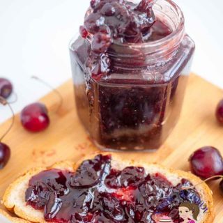 A jar of cherry jam and a piece of bread with jam.