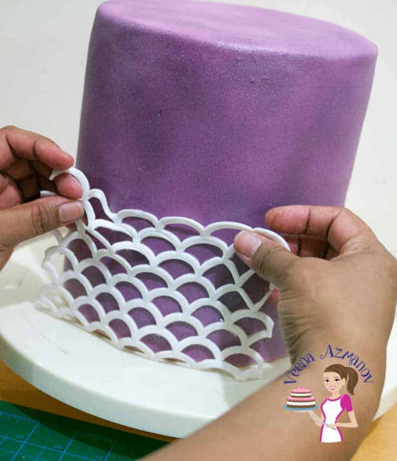 A person decorating a cake with sugar paste designs made with silicon mold.