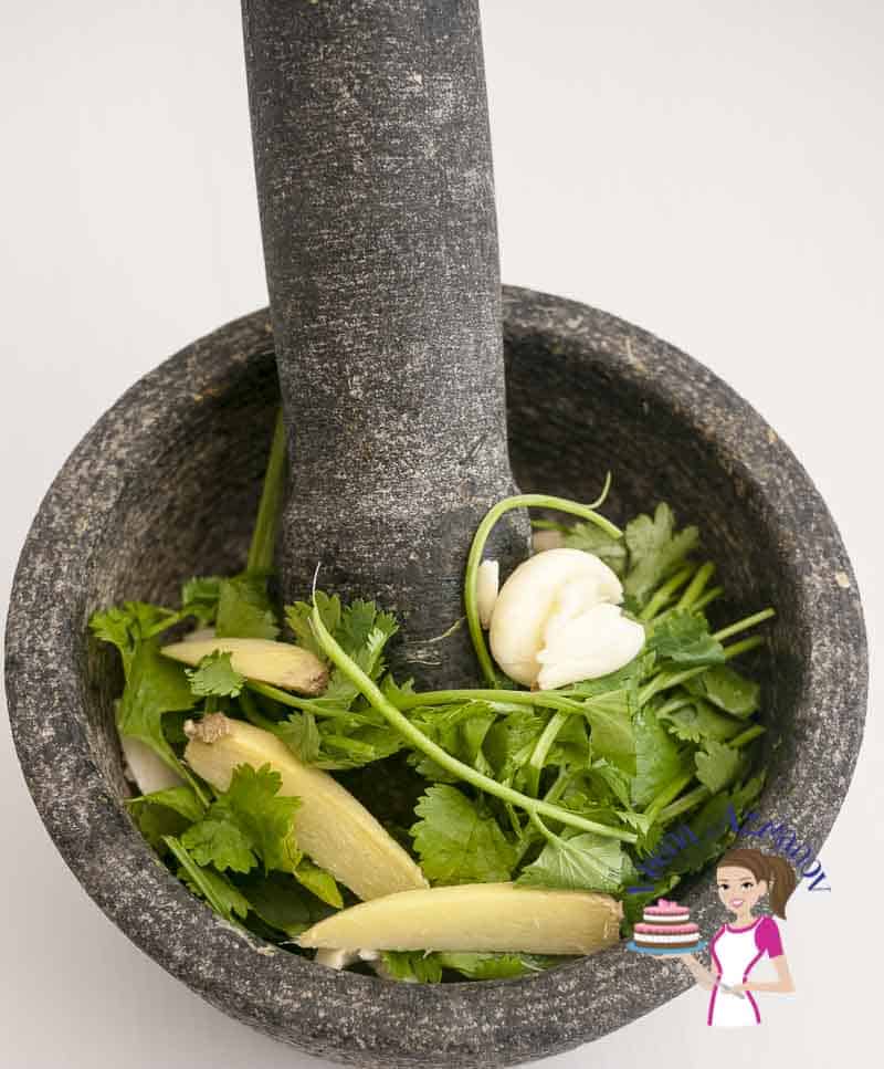 A mortar and pestle with fresh cilantro, ginger and garlic.