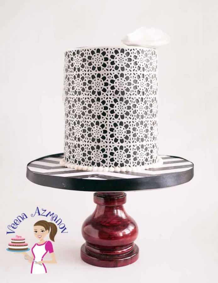 A black and white lace decorated cake on a stand.