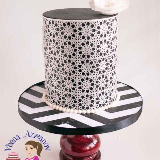 A black and white lace decorated cake on a stand.