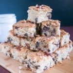 A stack of coconut cake squares on a wooden board.