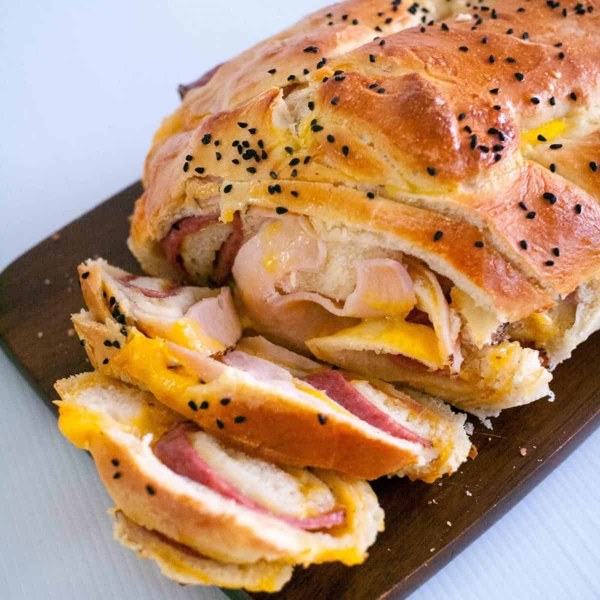 Sliced bread with ham and cheese on a wooden board.