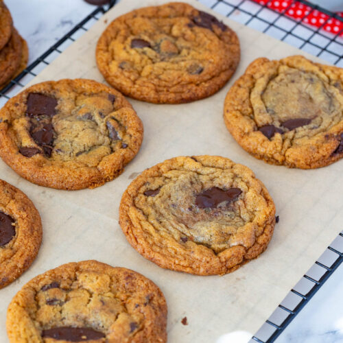 Thin crispy chocolate chip cookies on a wire rack.