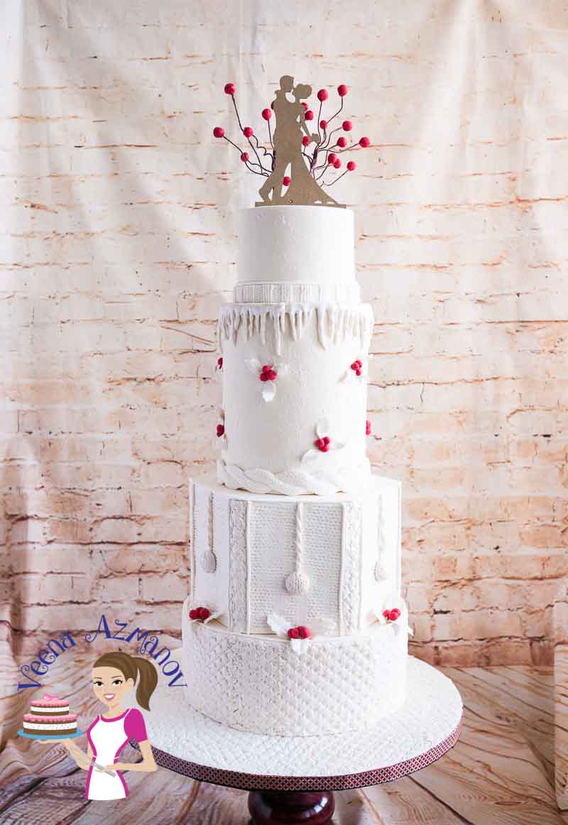 A Classic Winter Wedding Cake inspired by the knit wear. Nothing says winter better than winter clothing and this cake has it all in plenty.  All white cake with the effect of snow and a pop of red Christmas berries and leaves.