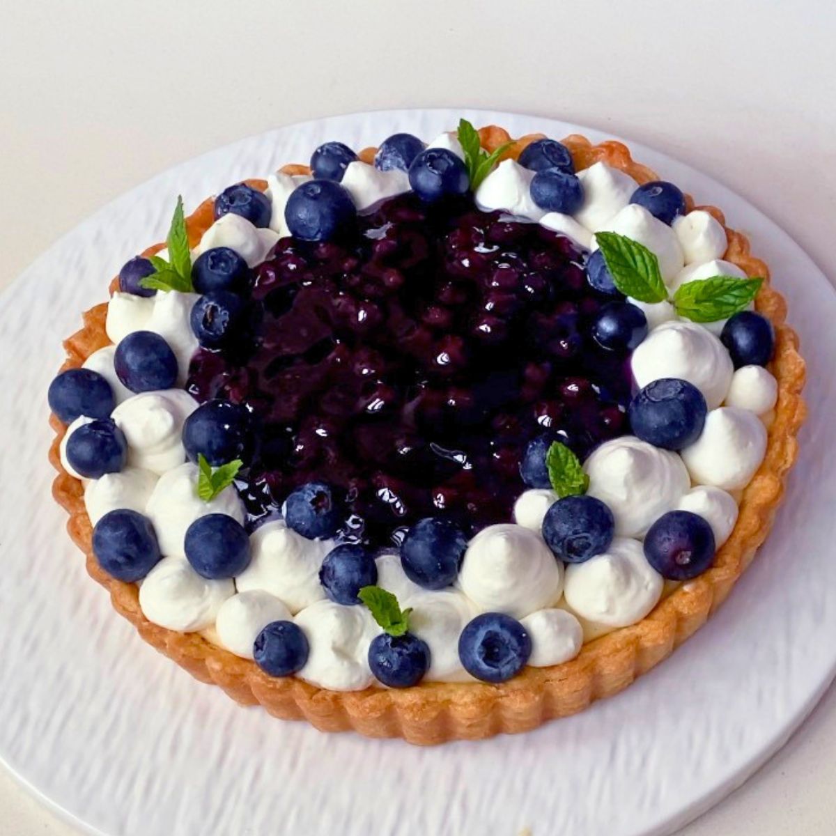 Frosted blueberry tart with custard filling and cream.