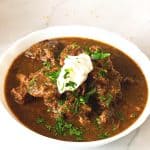A white bowl with beef goulash.