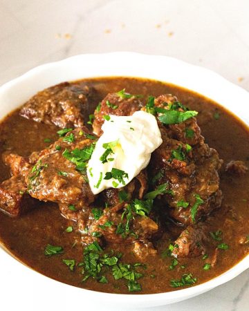 A white bowl with beef goulash.