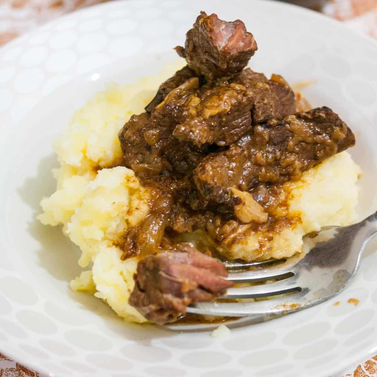 A plate of slow cooked beef with mashed potatoes.