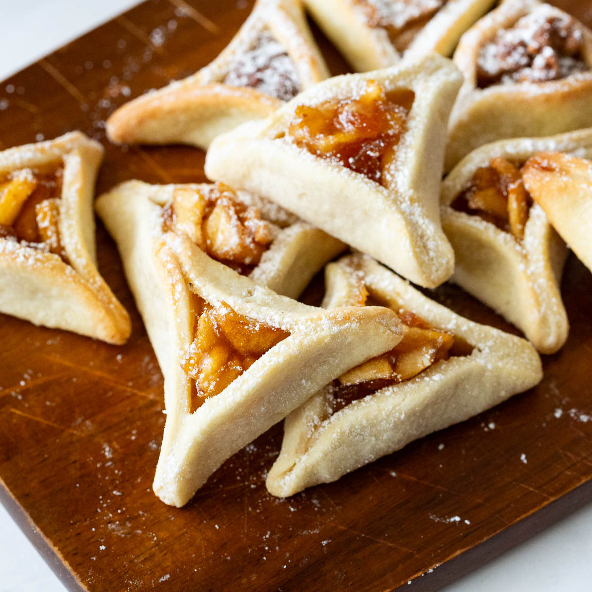 A Purim party is incomplete without Purim cookies and these dates Purim cookies are an absolute addiction. This simple, easy and effortless recipe for festive purim cookies also called hamentaschen or oznei haman are filled with naturally sweet dates and pecans then folded in a short bread cookie dough to get a traditional triangle shape. A stack of Jewish Hamantaschen Purim cookies is on the table.
