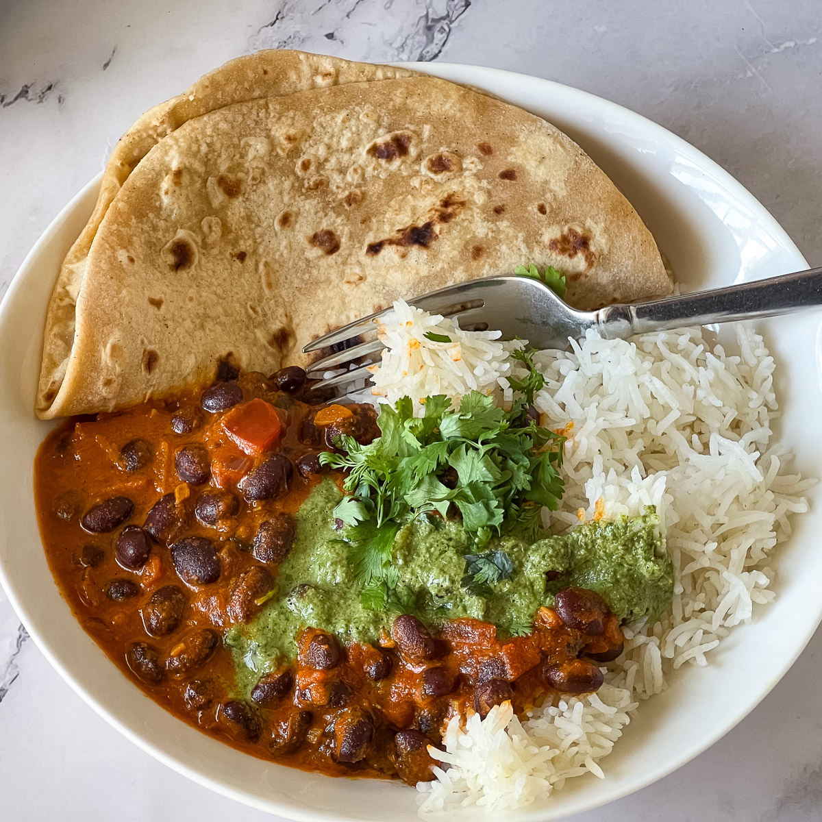 A white plate with rice chapati and kidney beans curry.