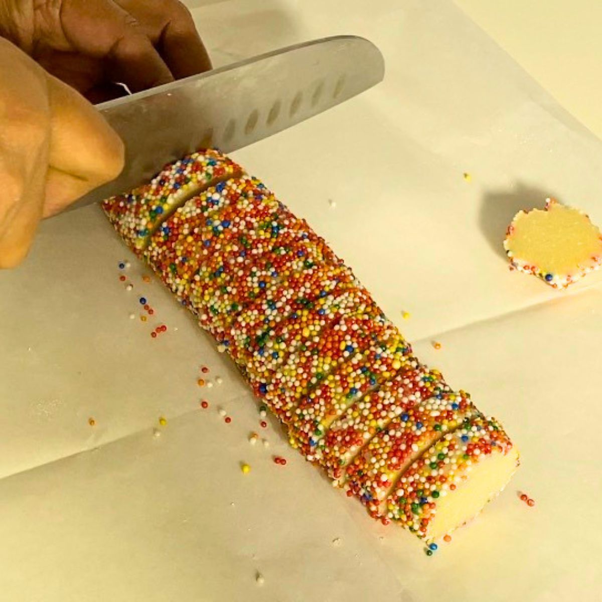 Cutting a log of sprinkle cookies on the wooden board.