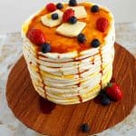 A pancake cake on a round wooden cake board.