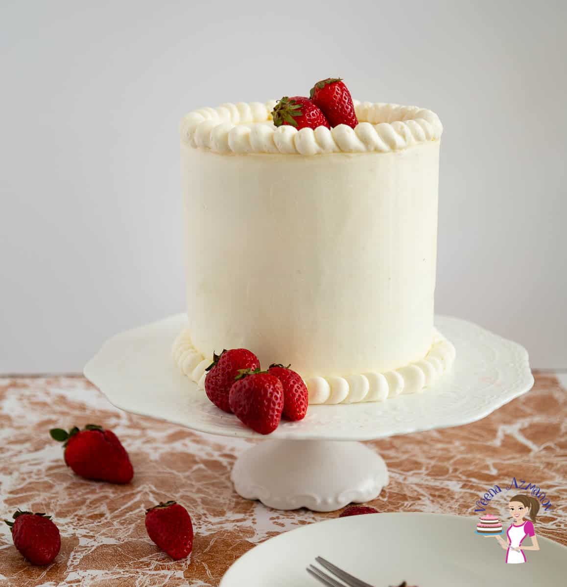 A frosted cake on a cake stand with fresh strawberries