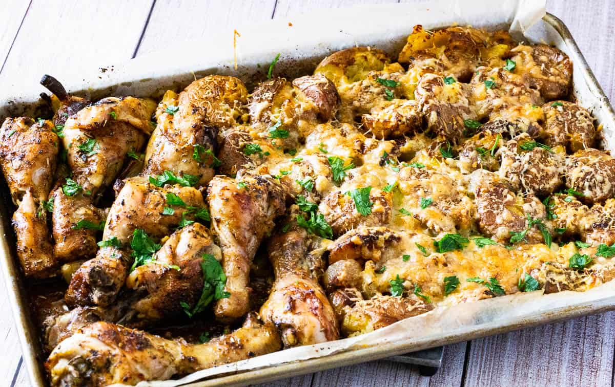 A sheet pan with roasted chicken and smashed potatoes.