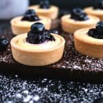 Mini tarts with cream cheese and blueberry filling a wooden board.