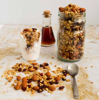 A jar filled with granola next to a glass of yogurt with granola on top.