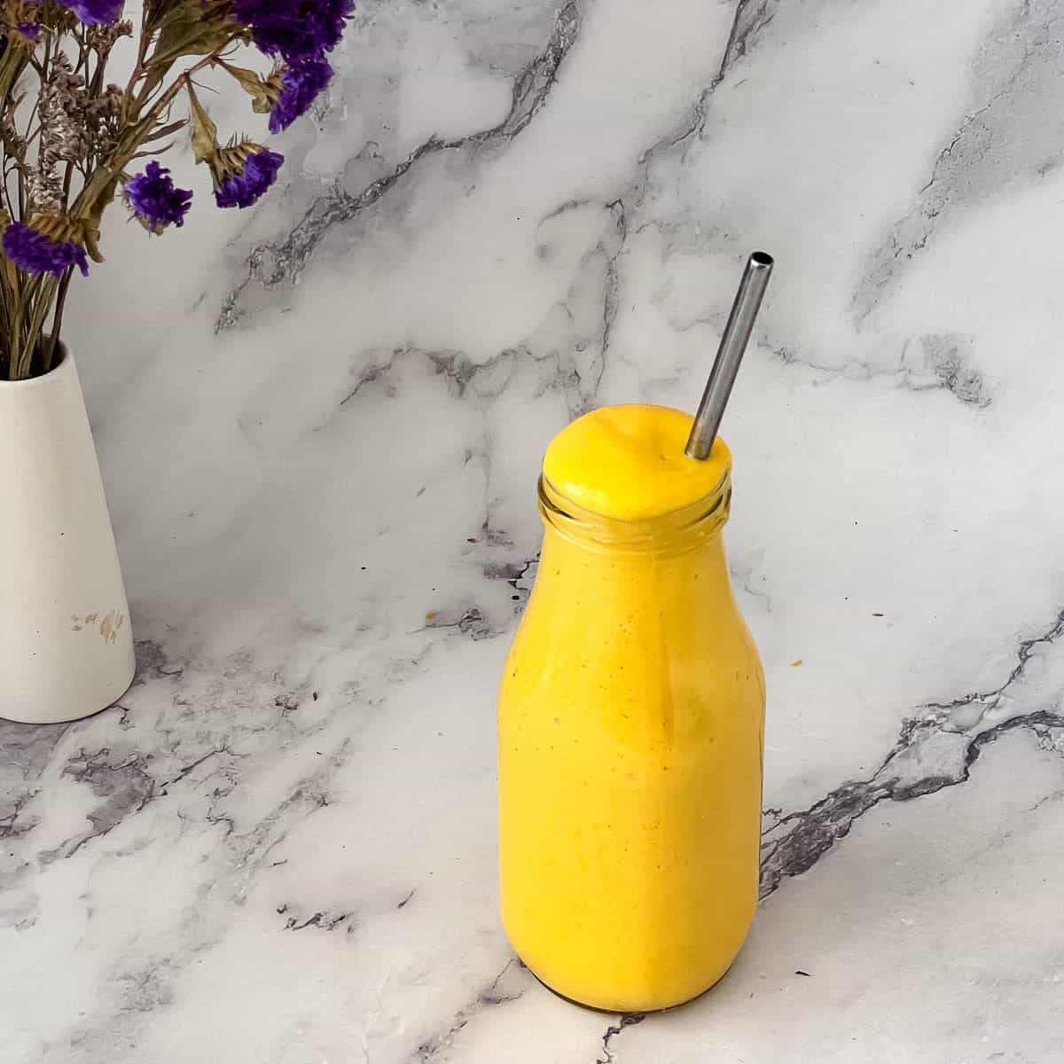 A glass bottle with mango smoothie.