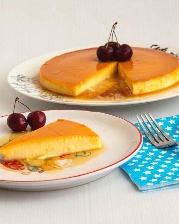 A slice of apricot flan on a plate with cherries.