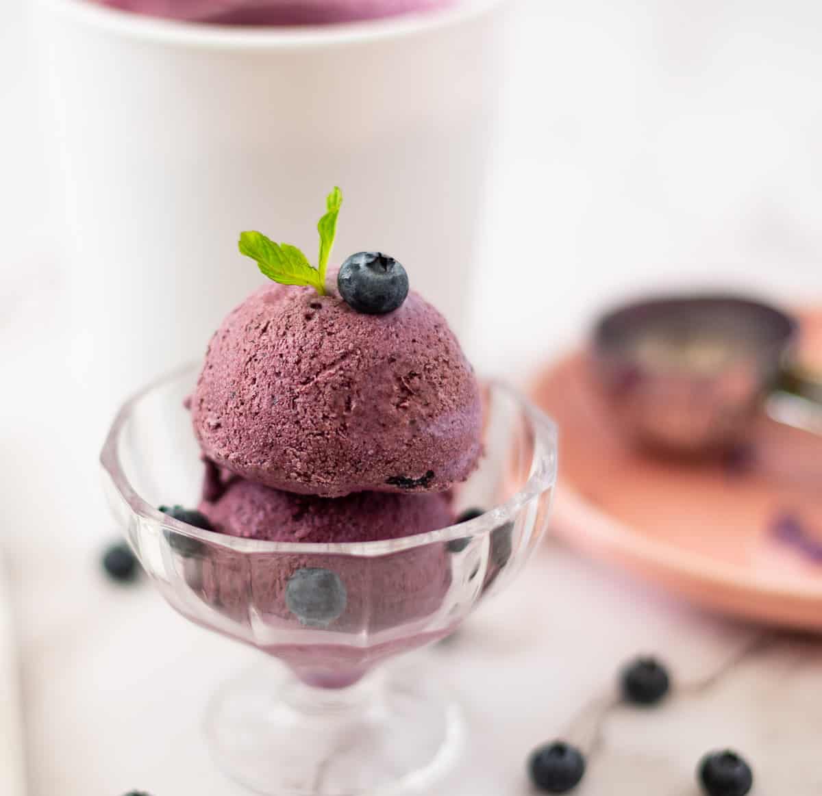 A glass bowl with blueberry ice cream scoops.
