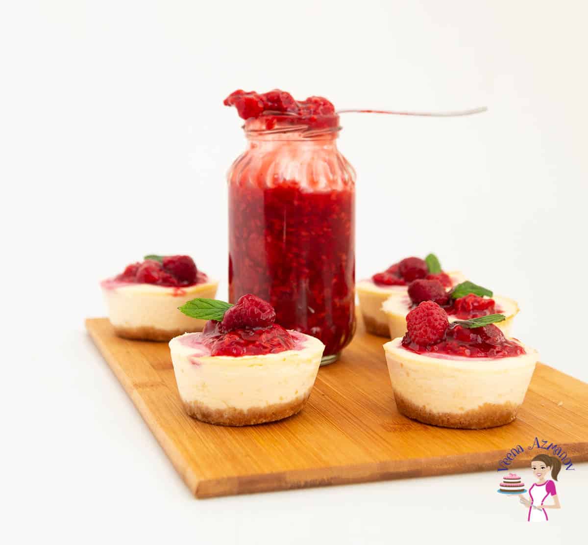 Mini raspberry cheesecakes on a table with a jar of raspberry filling.