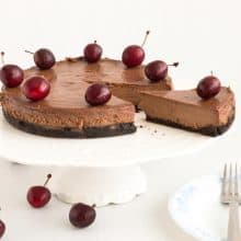 Sliced chocolate cherry cheesecake on a cake stand.