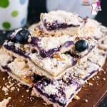 A stack of blueberry cake squares on a wooden board.