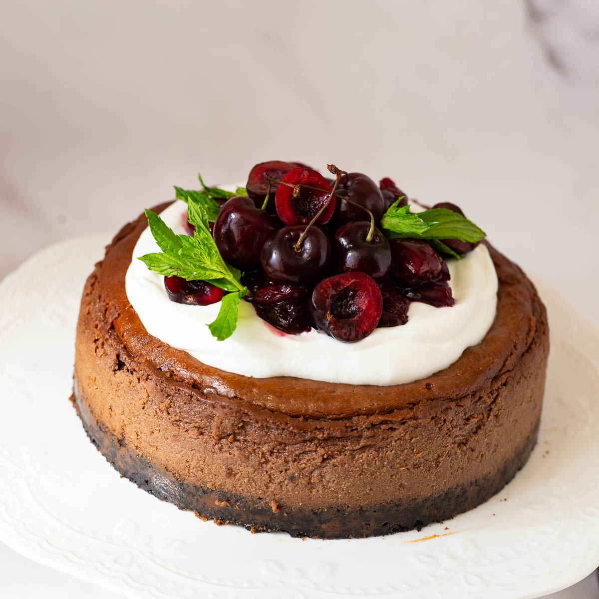 A chocolate cheesecake with whipped cream and cherry filling on a cake stand.