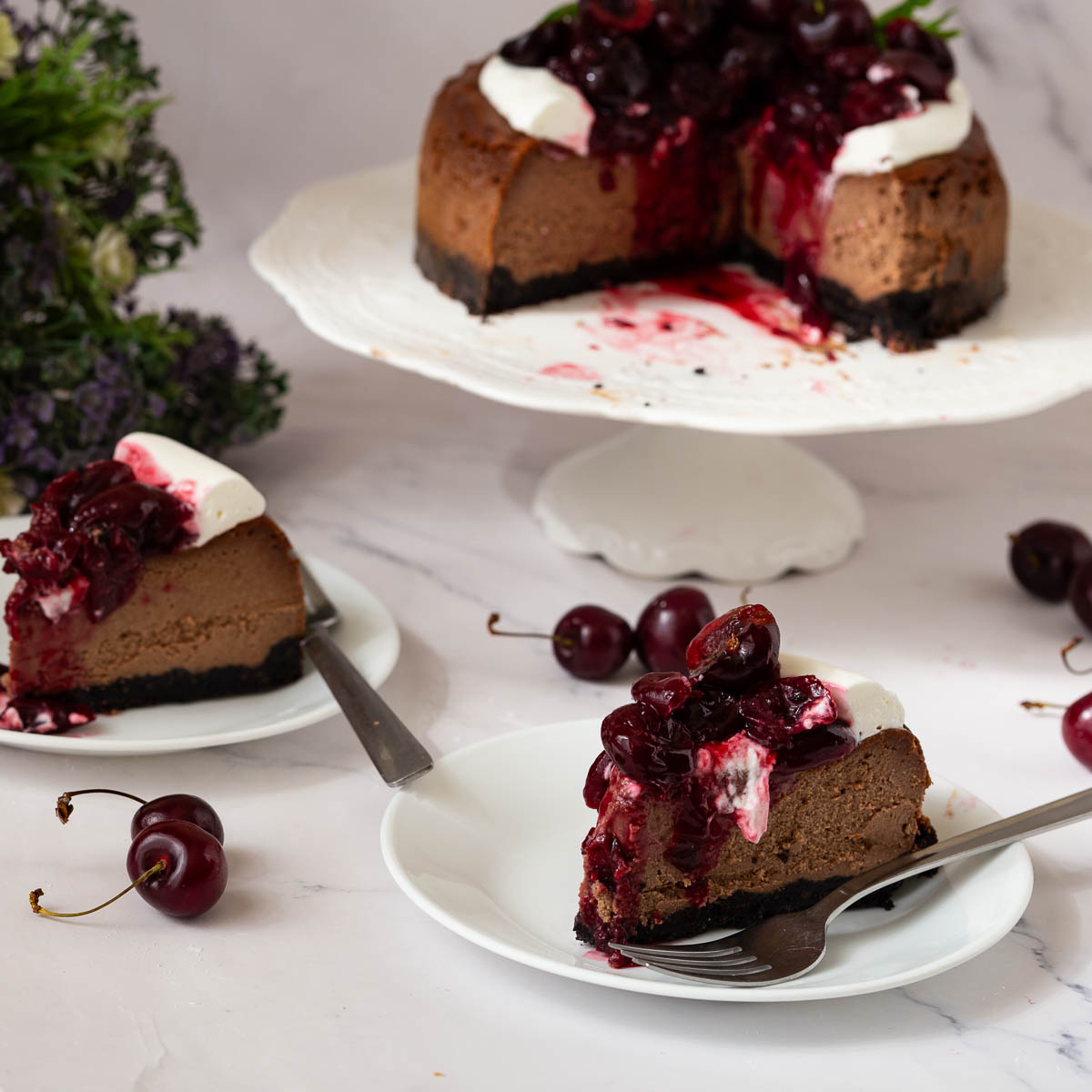Cake and slices of chocolate cherry cheesecake on a table.
