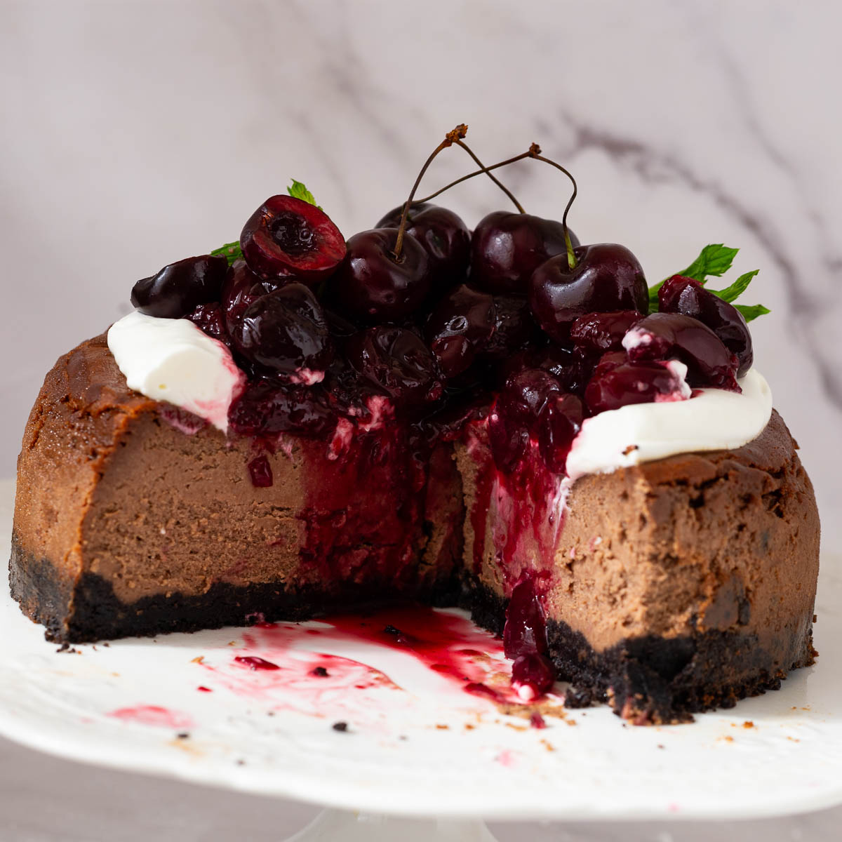 A Chocolate cheesecake topped with cherry pie filling on top of a cake stand.