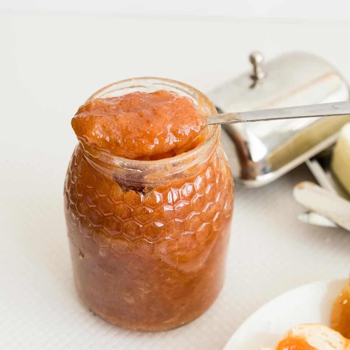 A jar and spoon with jam - peach plums.