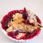 A ramekin and spoon with raspberry fruit crumble.